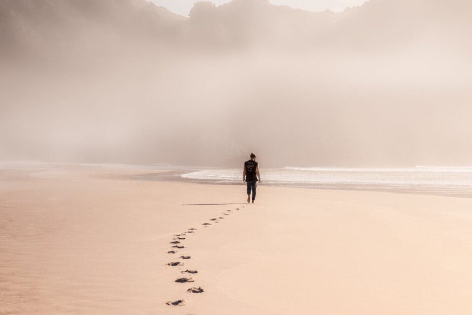 anonymous man walking on sandy seashore in misty weather