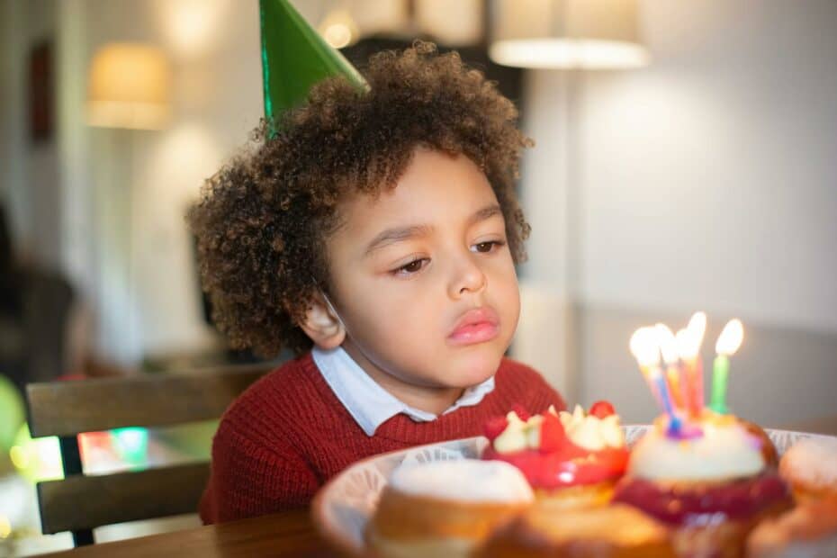 a boy wearing party hat looking at the lighted candles on the donut