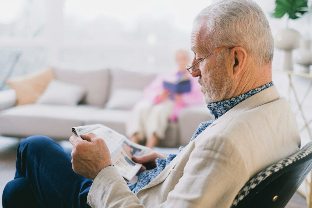 Elderly man in glasses reading newspaper at home with serene atmosphere.