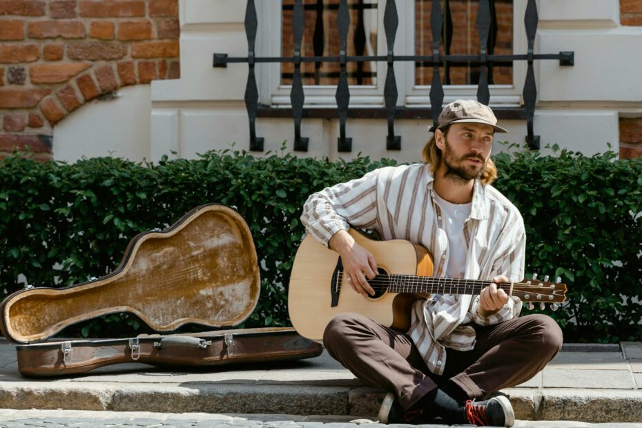 A street musician performs with an acoustic guitar, case open on the sidewalk, in a sunny urban setting.