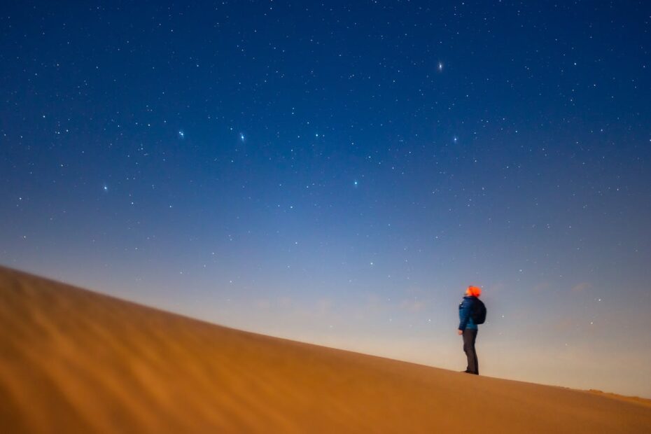 A lone person gazing at the starry night sky from a sand dune, evoking tranquility and wonder.