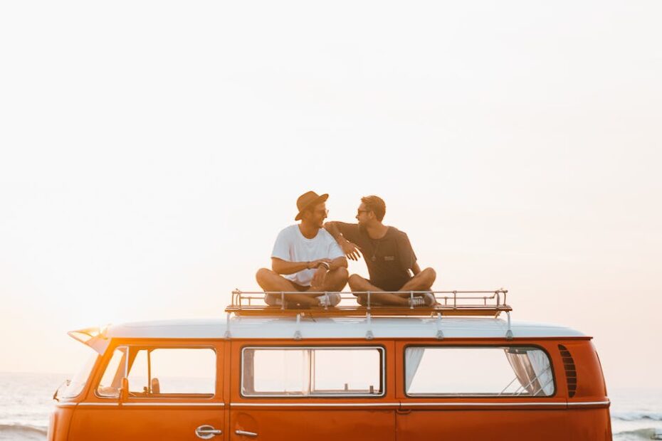 Silhouettes of full body faceless male friends in casual clothes resting on camper van roof and chatting in countryside in sunset time