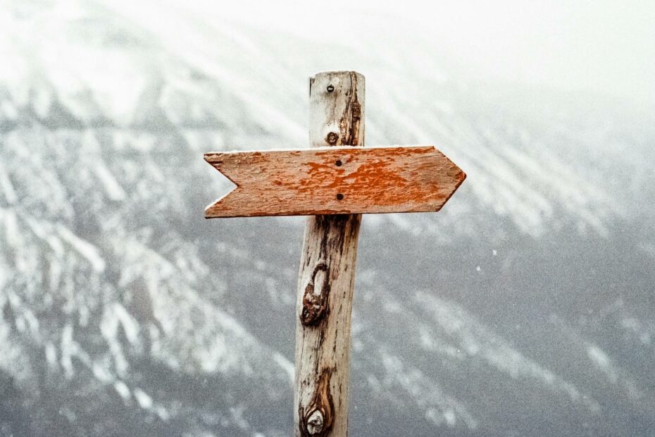 A wooden arrow signpost points the way amidst a snowy mountain landscape.