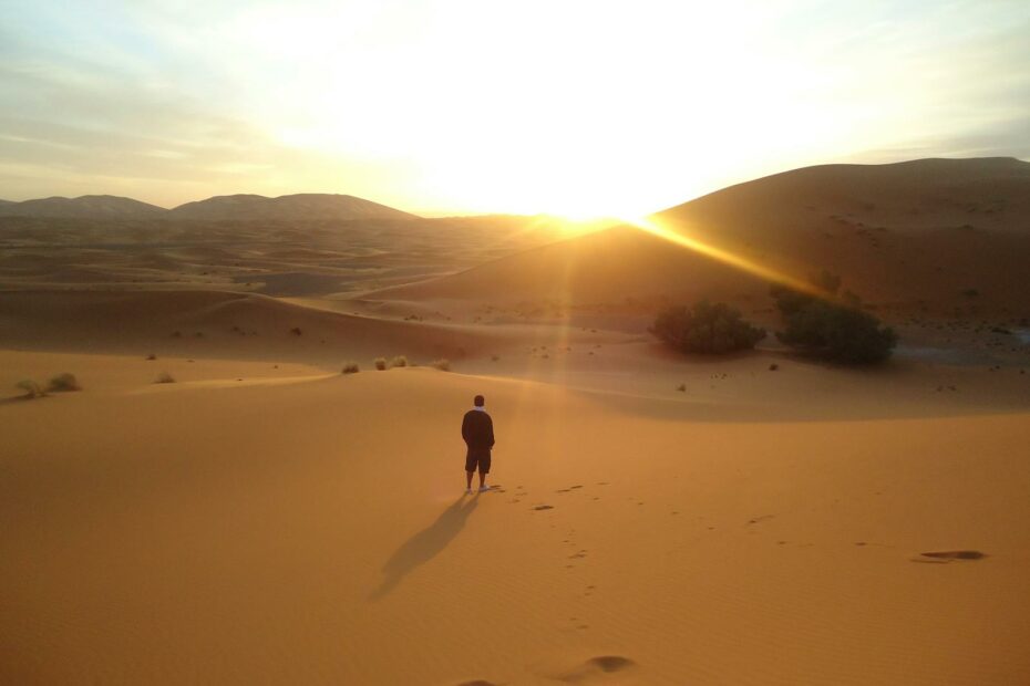 Silhouette of a man walking along sand dunes during a sunrise in the Sahara Desert.