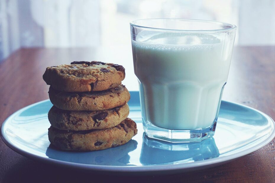 Close-up of chocolate chip cookies stacked beside a glass of milk on a blue plate.