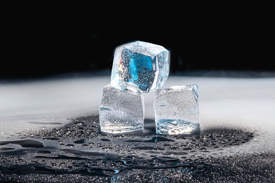 Three ice cubes melting on a black surface with water droplets.